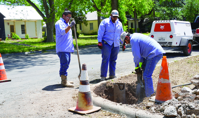 Anthony Perez (holding a shovel) and Greg Dehoyes look on as Daniel Chaves uses a jack hammer to remove a broken section of the water hydrant./ Photo by John Starkey